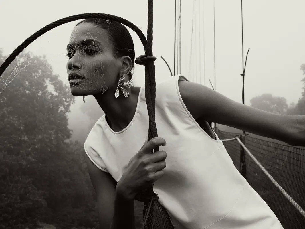 Model posing on a suspended bridge in a rainforest setting